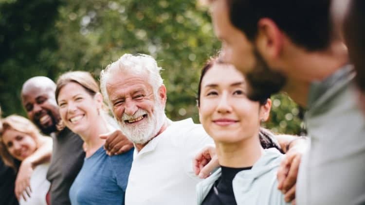 Diverse group of old and young with linked arms, smiling