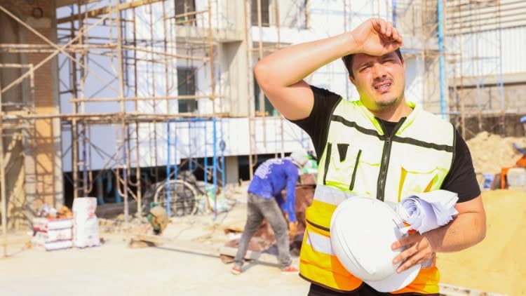 Heat stress at work—a political emergency building worker facing into the sun, suffering in the heat; site scaffolding in background