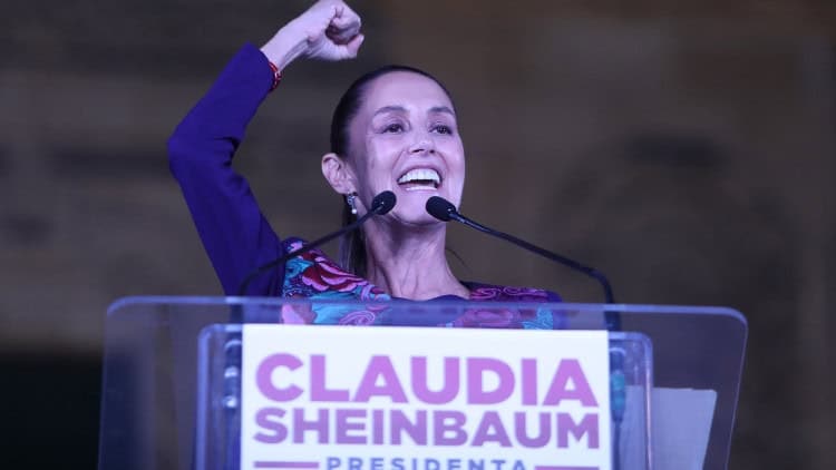 Neoliberalism is blocking green growth Woman behind 'Claudia Scheinbaum presidenta' podium raises fist in the air