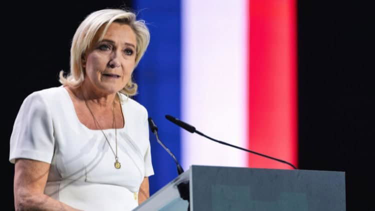 How to puncture the populist right in Europe Woman addressing microphone at podium with colours of French tricolour behind