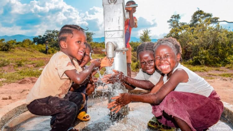 Development: better days could lie ahead (yes, really) Children laughing as they play around a well amid splashing waster from a tap.