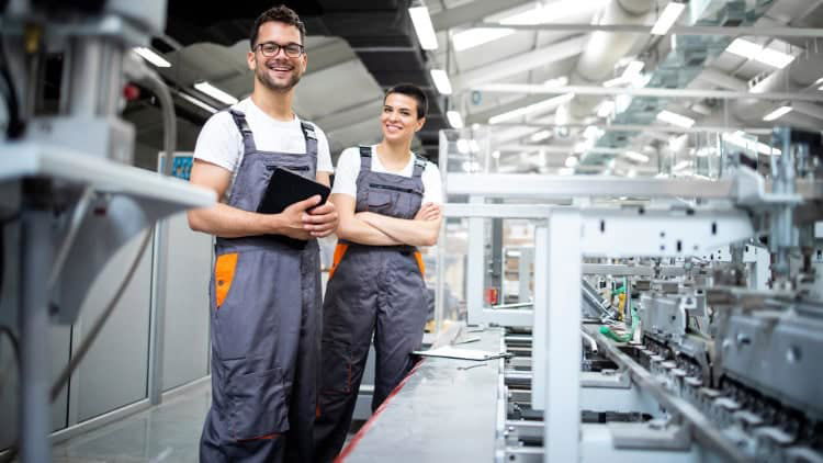 Two workers in dungarees looking relaxed in a manufacturing workshop