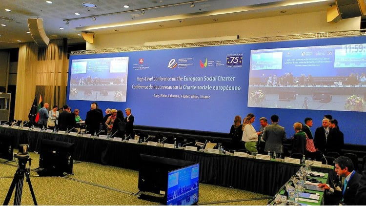 European Social Charter: France’s ‘overseas’ gap Conference participants chatting in front of big screens and the title of the event in English and French