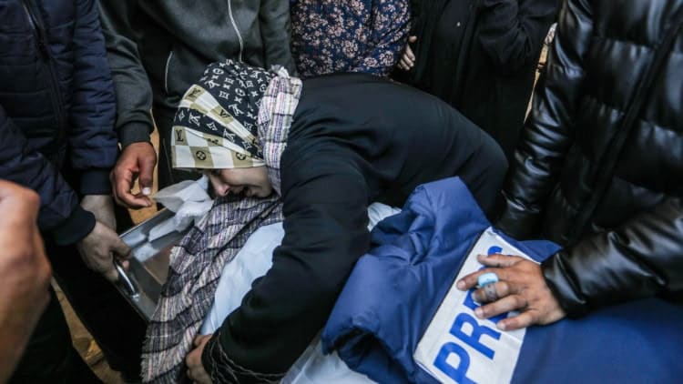 Gaza: a war against press freedom Woman crying among mourners over body of man, with his blue 'PRESS' jacket lying on top of him
